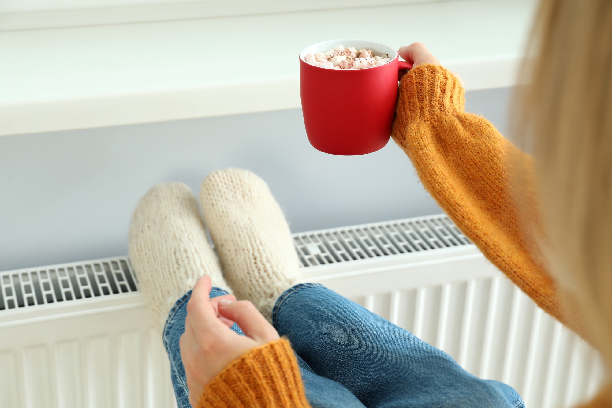 Concept of heating season with girl sitting near radiator